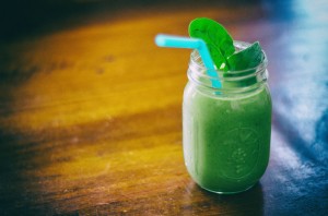 A glass jar containing a green smoothie with a leaf garnish and a straw.
